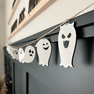 laser cut ghosts hanging from a jute twine string on a green paneled wall