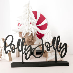 The phrase "holly jolly" cut in black and in a black stand sits in front of two white washed wood stars, a white plant stand that holds a small white christmas tree. In the far background is a peppermint candy circle. It is really cute.