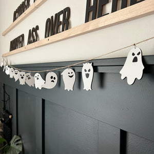 laser cut ghosts hanging from a jute twine string on a dark green paneled wall