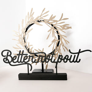 The phrase "Better not pout' stands in front of a wreath stand holding a gold olive branch wreath