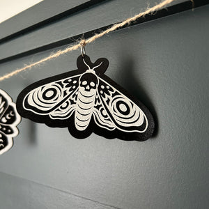 white moth on a black background laser cut and hanging on a jute twine garland