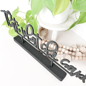 The little word stand in black standing in front of a plant stand with a wood bead garland laying in a pile