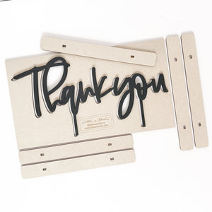 The phrase &quot;thank you&quot; cut out and painted black. It is laying on the cut out pieces from the listing.