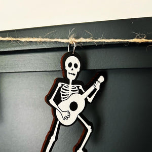 skeleton holding a guitar hangs from a jute string with a silver finding
