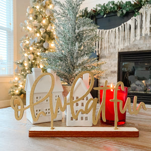 The phrase "oh what fun" cut in natural wood standing on a coffee table in front of christmas decor