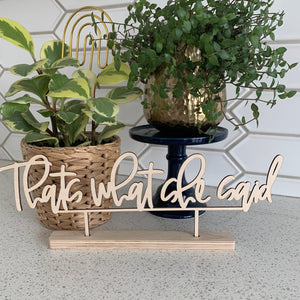 The phrase "that's what she said" in unfinshed wood. It is sitting on a quartz countertop with plants in the background.